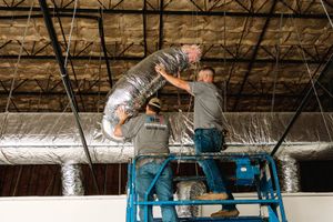R2 crew installing ductwork from a lift in a commercial building